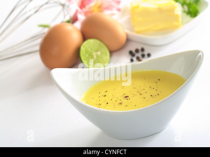 Salsa Olandese con pepe nero e gli ingredienti (burro, uovo, limone) della salsa nel retro Foto Stock