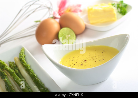 Salsa Olandese con pepe nero, asparagi sul lato e gli ingredienti (burro, uovo, limone) della salsa nel retro Foto Stock