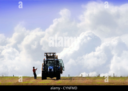 Un agricoltore si stringe una corda sopra il suo rimorchio delle balle di fieno nel GLOUCESTERSHIRE REGNO UNITO Foto Stock