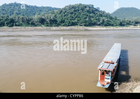 LUANG PRABANG, Laos - le acque marroni del fiume Mekong scorrono oltre Luang Prabang nel Laos centrale, con lussureggianti colline visibili sulla sponda opposta. Un sampan coperto in legno è ormeggiato in basso a destra della cornice, illustrando il trasporto fluviale tradizionale nella regione. Foto Stock