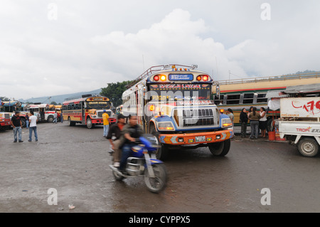 ANTIGUA GUATEMALA, Guatemala — Chicken Buses e una moto dietro il Mercado Municipal (mercato cittadino) ad Antigua, Guatemala. Da questo ampio interscambio centrale di autobus, i percorsi si irradiano attraverso il Guatemala. Spesso verniciati con colori vivaci, gli autobus a base di pollo sono scuolabus americani adattati e forniscono un mezzo di trasporto economico in tutto il paese. Foto Stock