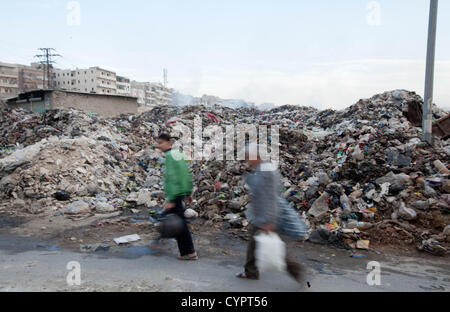 8 novembre 2012 - Aleppo, Siria: gli uomini a piedi da una discarica di rifiuti in Geser Hag. Le persone nella città sono state bruciando il cestino a una velocità crescente. Foto Stock