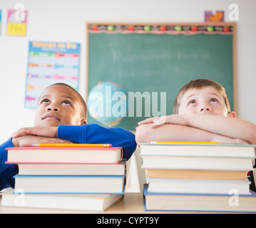 Gli studenti poggiando su pile di libri in aula Foto Stock