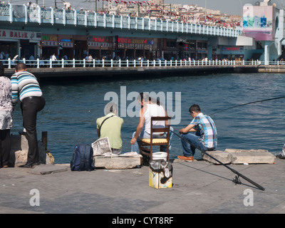 La pesca nei pressi del Ponte di Galata Istanbul in Turchia, una delle attività più popolari, compagnia uomini seduti sulla banchina con attrezzature per la pesca Foto Stock