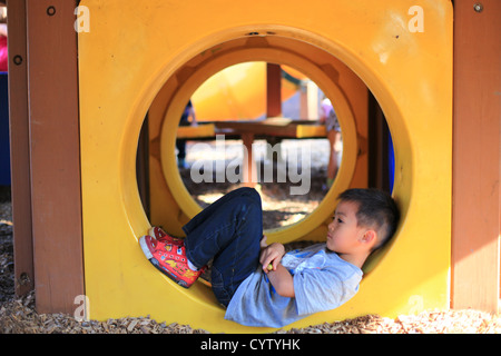 Il Toddler ragazzo disteso tranquillamente sul retro all'interno di un tubo nel parco, perso nel pensiero Foto Stock