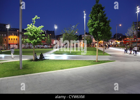 Gordon generale posto, Woolwich, UK. Moderno e paesaggistici town square di notte con ampi marciapiedi, sedili, alberi e aree di erba. Foto Stock