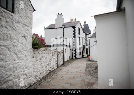 BEAUMARIS, Anglesey, Galles, un vicolo nella città di Beaumaris, caratterizzato da edifici bianchi con dettagli neri. La stretta strada è fiancheggiata da strutture tradizionali che riflettono il carattere architettonico di questa comunità di Anglesey. Beaumaris si trova sull'isola di Anglesey al largo della costa settentrionale del Galles. La città è ampiamente conosciuta per il suo castello medievale, costruito alla fine del XIII secolo come parte della conquista del Galles da parte di Edoardo i. L'insediamento si sviluppò intorno al castello e conserva gran parte della sua struttura storica delle strade. Beaumaris è una destinazione popolare per i visitatori che esplorano Ang Foto Stock