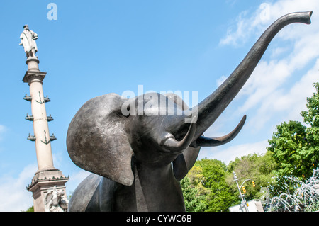 NEW YORK, NY - uno dei più vita-dimensioni delle sculture di elefanti e altri animali selvatici che compongono una mostra d'arte pubblica distribuiti sulla lunghezza di Broadway a New York. Il lavoro è da artista Peter Woytuk. In fondo è la alta colonna su cui si erge la statua di Cristoforo Colombo. Foto Stock