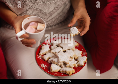 Primo piano sulla donna mangiare biscotti di Natale e di bere cioccolata calda con marshmallows Foto Stock