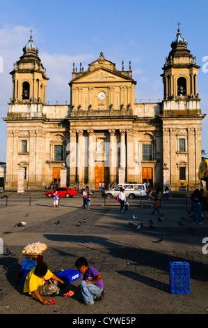 CITTÀ DEL GUATEMALA, Guatemala — la Catedral metropolitana neoclassica domina il lato orientale del Parque Central a città del Guatemala. I due campanili della cattedrale si innalzano sopra gli edifici circostanti, mentre la vivace piazza di fronte presenta la fontana ornata e la gente del posto, esemplificando il mix della città tra il patrimonio coloniale e la vita urbana moderna. Foto Stock