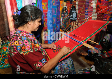 ANTIGUA GUATEMALA, Guatemala - Una donna Maya dimostra la tradizionale tessitura del telaio dello schienale, creando tessuti vivaci. Le sue mani manipolano abilmente fili colorati, producendo intricati motivi che riflettono tecniche secolari e simbolismo culturale, mentre huipiles finiti e altri tessuti sono appesi sullo sfondo. Foto Stock