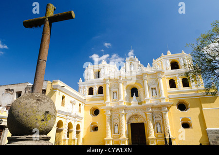 Il colore giallo brillante chiesa e convento della Madonna della Misericordia (Iglesia y Convento de Nuestra Senora de la Merced) in Antigua, Guatemala, con croce di ferro a sinistra del telaio e chiesa gialla in background. Foto Stock