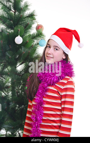 Ritratto di giovane ragazza che indossa beanie, in piedi vicino ad albero di natale, contatto visivo, colpo verticale Foto Stock