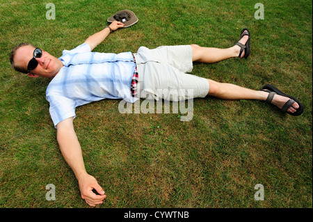 Uomo in pantaloncini corti che giace flat-out sull'erba Foto Stock