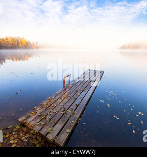 Piccolo molo in legno sul lago ancora in bright autunnale mattinata nebbiosa Foto Stock