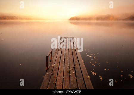 Piccolo molo in legno sul lago ancora in autunnale mattinata nebbiosa con Rising Sun Foto Stock