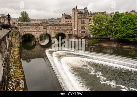 BATH, Regno Unito — lo storico Pulteney Bridge attraversa il fiume Avon nel centro di Bath, Somerset. In primo piano, i gradini artificiali del livello dell'acqua per il canale creano acqua bianca, aggiungendo una vista panoramica e dinamica. Pulteney Bridge, completato nel 1774, è uno dei quattro ponti al mondo con negozi che fiancheggiano entrambi i lati. Foto Stock