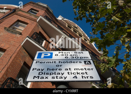I titolari di autorizzazioni e pagare nei parcheggi a firmare in Hammersmith, Londra, Inghilterra, con blocco di dimora in background Foto Stock