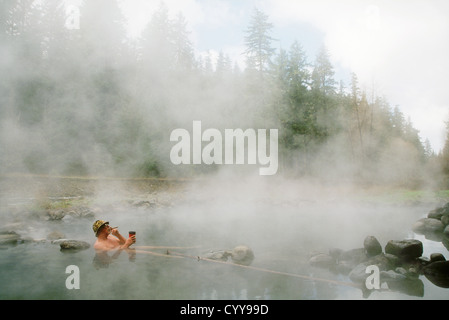 Uomo con cigar & caffè immersione in piscina a McCredie Hot Springs lungo Salt Creek; Willamette National Forest, Oregon. Foto Stock