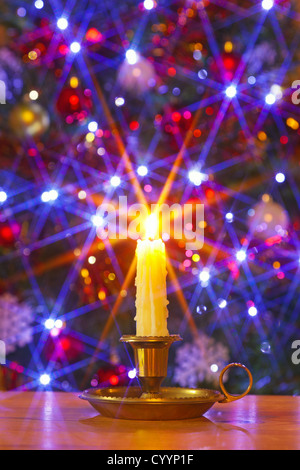 Un gocciolamento candela di cera in ottone titolare contro un albero di Natale con le decorazioni e le luci fairy Foto Stock