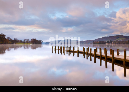 Un pontile sul Coniston Water nel distretto del lago, Cumbria, Inghilterra all'alba con nebbia in aumento e riflessioni Foto Stock