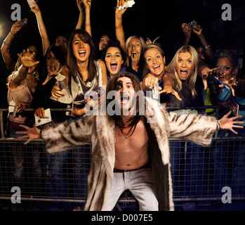 Ritratto di giovane uomo in pelliccia urlando con pubblico entusiasta in background Foto Stock