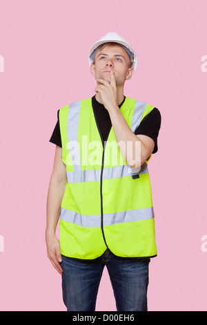 Considerato giovane lavoratore edile che guarda lontano su sfondo rosa Foto Stock