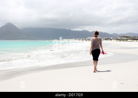 La donna a piedi lungo la spiaggia di Kommetjie con un imminente tempesta in background Foto Stock