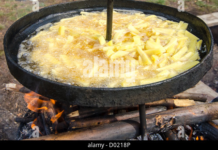 Patate fritte frittura in olio bollente in un grande calderone, sul fuoco, per esterno Foto Stock