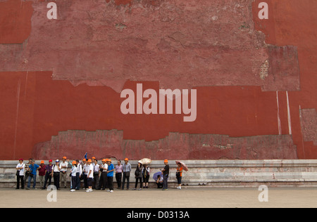 Un gruppo di turisti in piedi in linea di fronte una grande parete rossa al di fuori della Città Proibita di Pechino, Cina. Foto Stock