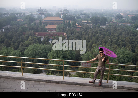 Un turista cinese con un ombrello rosa in posa per le fotografie su un lungomare al di sopra della Città Proibita di Pechino, Cina. Foto Stock