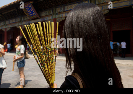 Una donna holding bastoncini di incenso prima di pregare presso il Tempio Lama a Pechino in Cina. Foto Stock