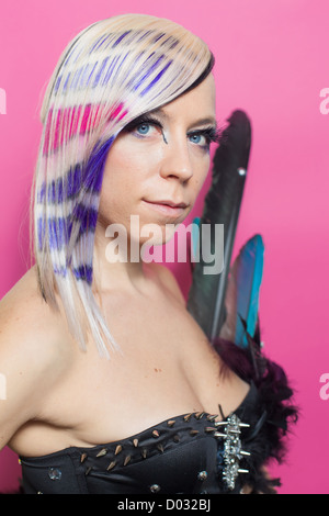 Donna con piume e multicolori per i capelli e gli occhi blu su sfondo rosa Foto Stock