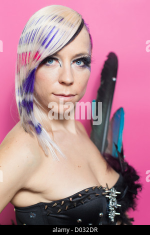 Donna con piume e multicolori per i capelli e gli occhi blu su sfondo rosa Foto Stock