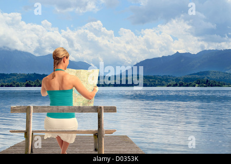 Una giovane donna la lettura di una mappa seduta su una panchina di fronte a un lago Foto Stock