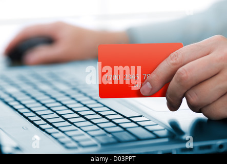 Uomo con la carta di credito in mano e immettendo il codice di protezione utilizzando la tastiera del notebook Foto Stock