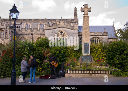 Busker gioca con il memoriale di guerra di fronte alla chiesa di San Giovanni Battista in Glastonbury Foto Stock