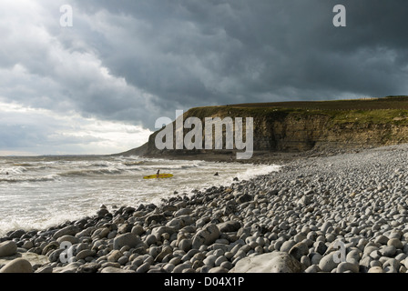 I surfisti e spiaggia di ghiaie e drammatiche scogliere Jurassic sotto un cielo tempestoso a Southerndown nel Galles del Sud. Foto Stock