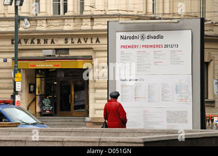 Praga, Repubblica Ceca. Narodni (street) Donna che guarda al Teatro Nazionale programma - Café Slavia dietro Foto Stock