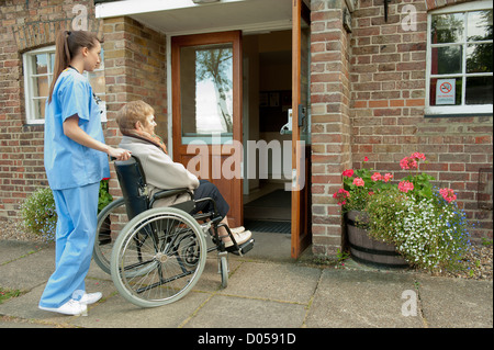 Infermiere/medici spingendo anziani paziente di sesso femminile in una sedia a rotelle verso l ingresso dell ospedale o casa di cura. Foto Stock