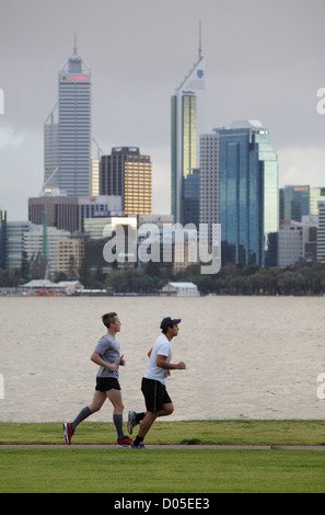 Due uomini jogging sul percorso accanto al fiume con la città sullo sfondo. Foto Stock