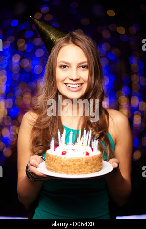 Ritratto di gioiosa ragazza con torta di compleanno con candele e guardando la fotocamera a parte Foto Stock