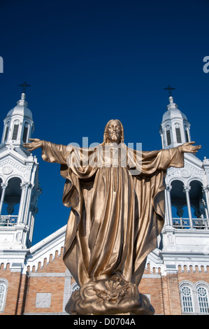 Statua d'oro di Gesù Cristo nella parte anteriore della Chiesa Cattolica con vivid blue sky in background. Foto Stock