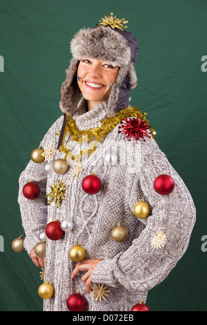 Piuttosto giovane donna sorridente con orgoglio che si presentano come un albero di Natale decorato, funny xmas studio shot contro uno sfondo verde Foto Stock