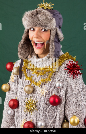 Carino giovane donna entusiasta di ridere in posa come un albero di Natale decorato, funny xmas studio shot contro uno sfondo verde Foto Stock