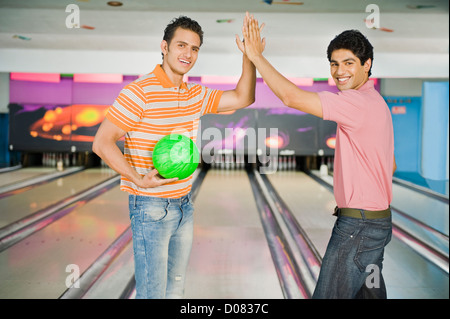 Due giovani uomini che danno alta cinque in una pista da bowling Foto Stock