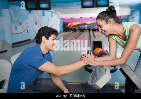 Giovane uomo seduto vicino al pannello di controllo e una giovane donna tenendo la sua mano in una pista da bowling Foto Stock