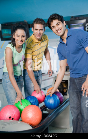 Due giovani uomini e una giovane donna che mantiene le palle da bowling in un impianto da bowling Foto Stock