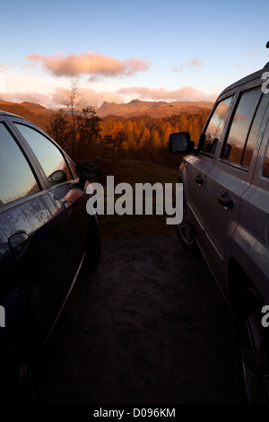 Due veicoli parcheggiati fino la mattina presto a guardare il tramonto su Tarn Hows e maggiore Langdale, Lake District inglese, Regno Unito Foto Stock