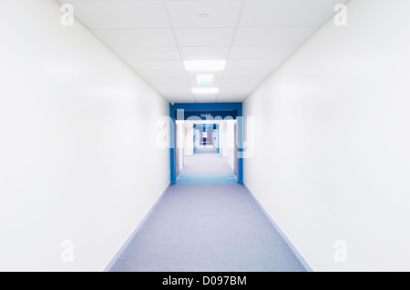 Vista lungo un luminoso corridoio bianco ad una sezione con pareti blu in una moderna scuola secondaria. Foto Stock